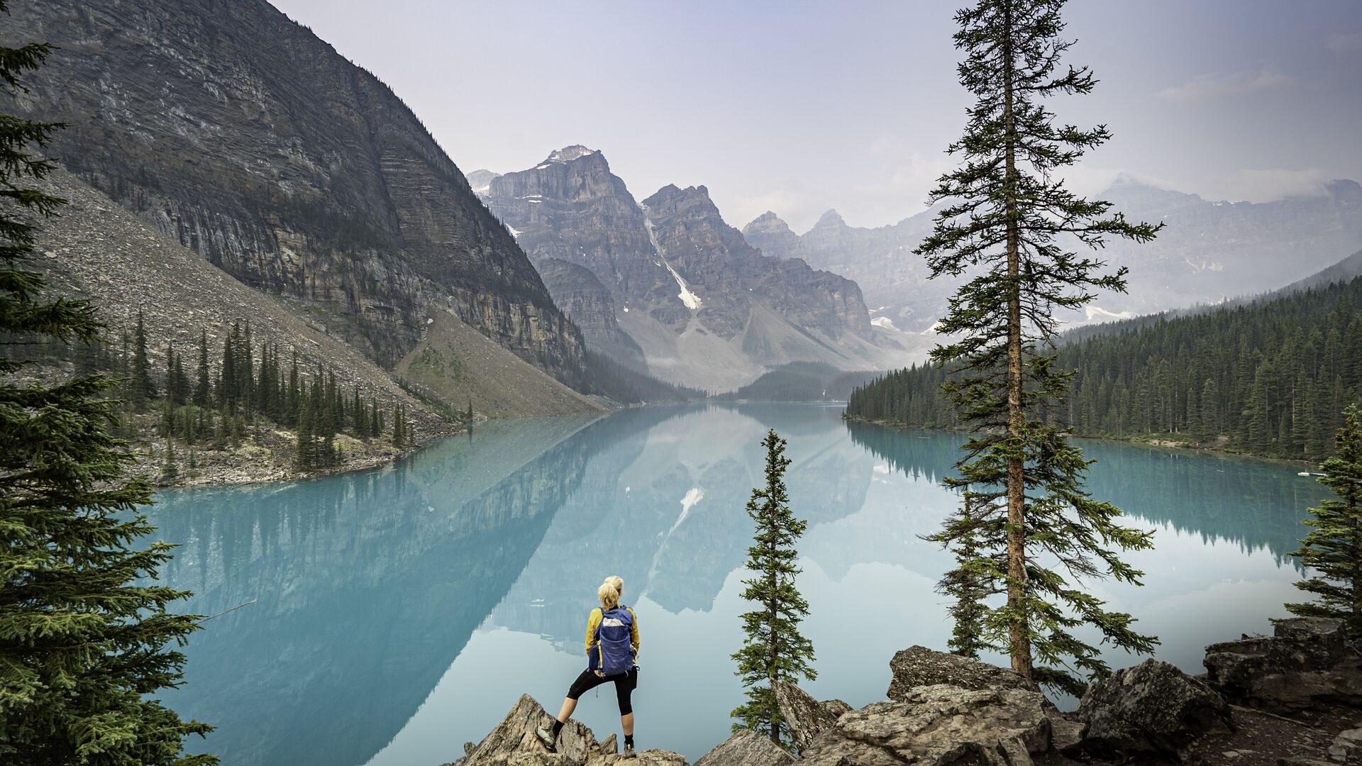 A visitor standing beside the turquoise water of Moraine Lake, with mountains beyond