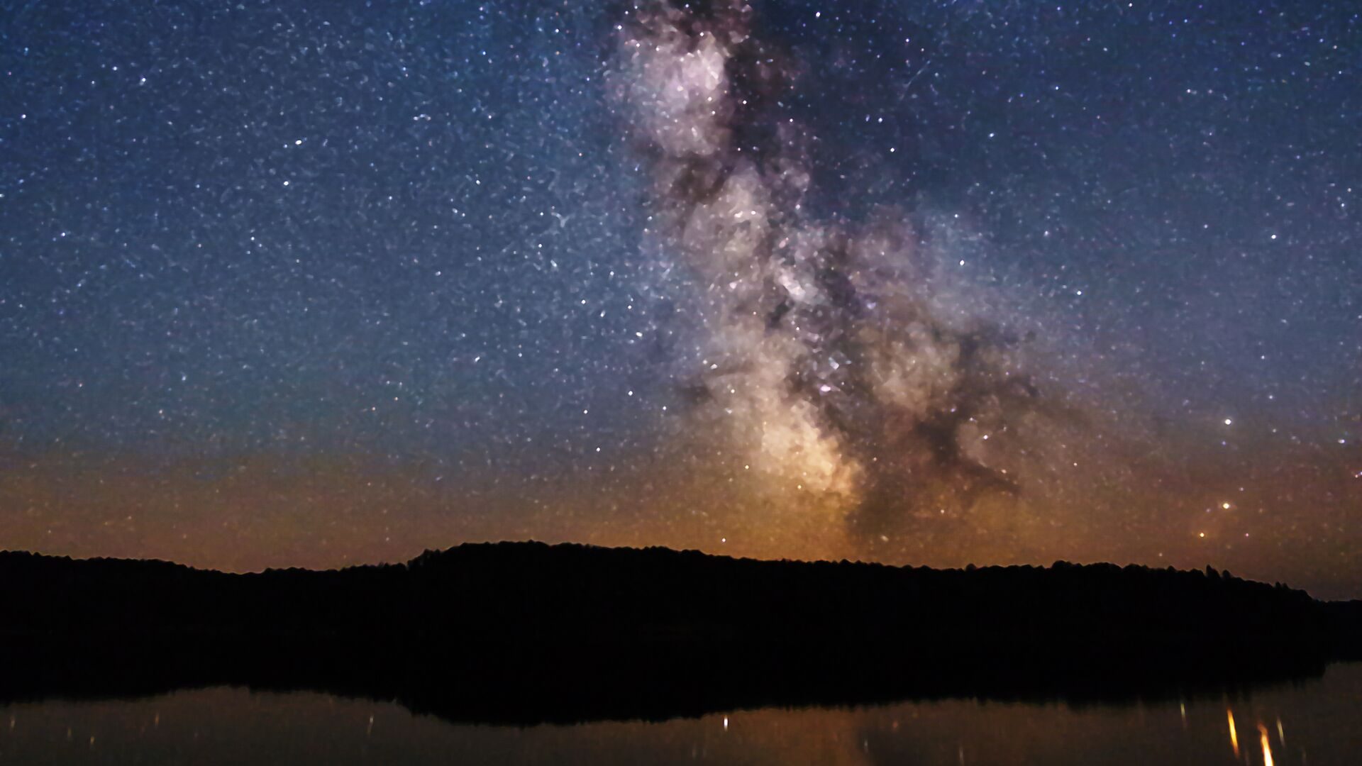 The Milky Way over a dark lake shore at night