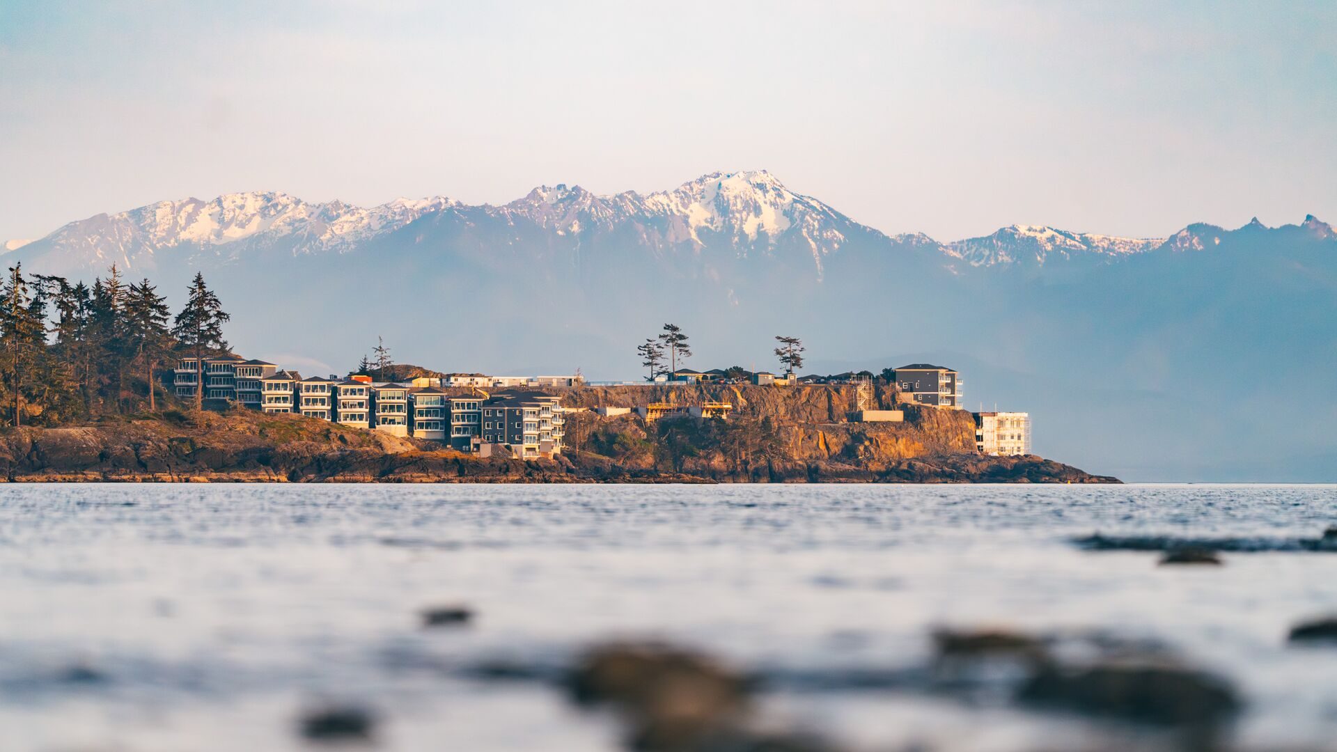 A seaside lodge on a rocky headland with snow-capped mountains across the water