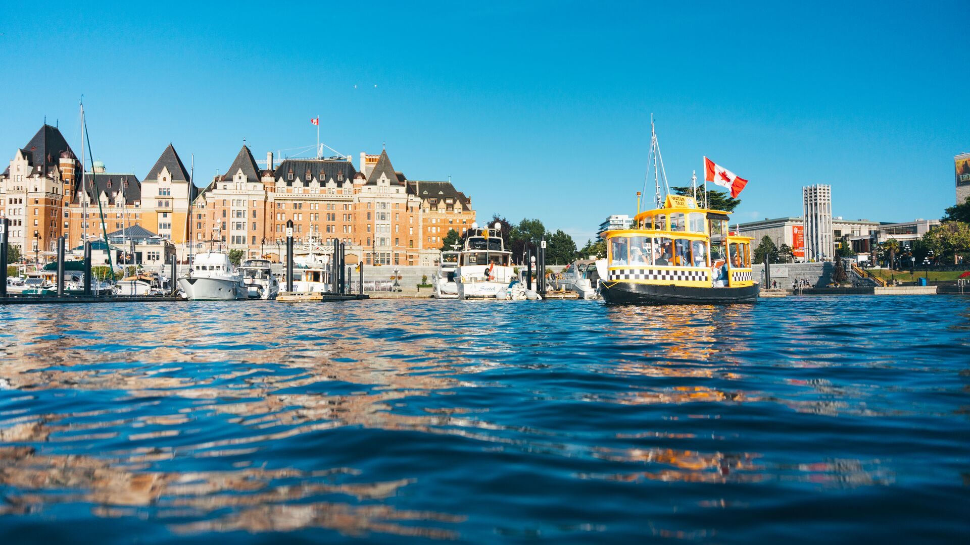 A harbour ferry crossing the blue water of Victoria's Inner Harbour in front of Fairmont Empress