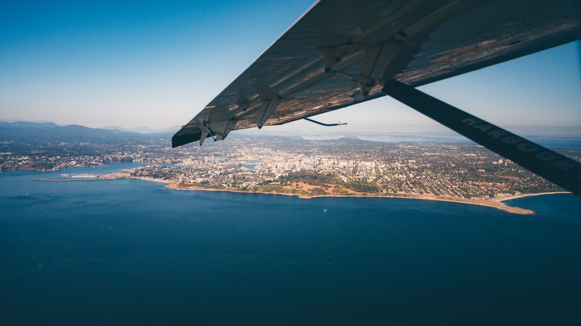 The wing of a floatplane over the water and city shoreline below
