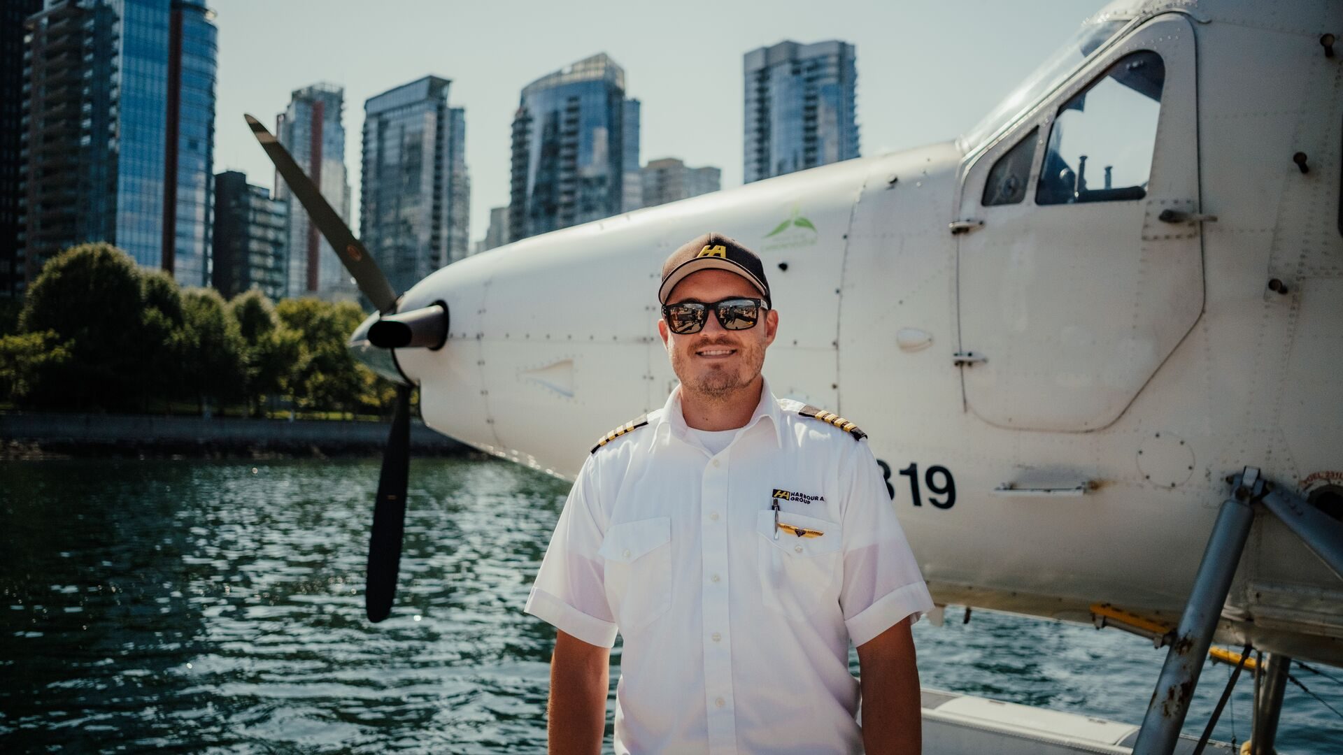 A smiling pilot beside a floatplane on the Vancouver waterfront