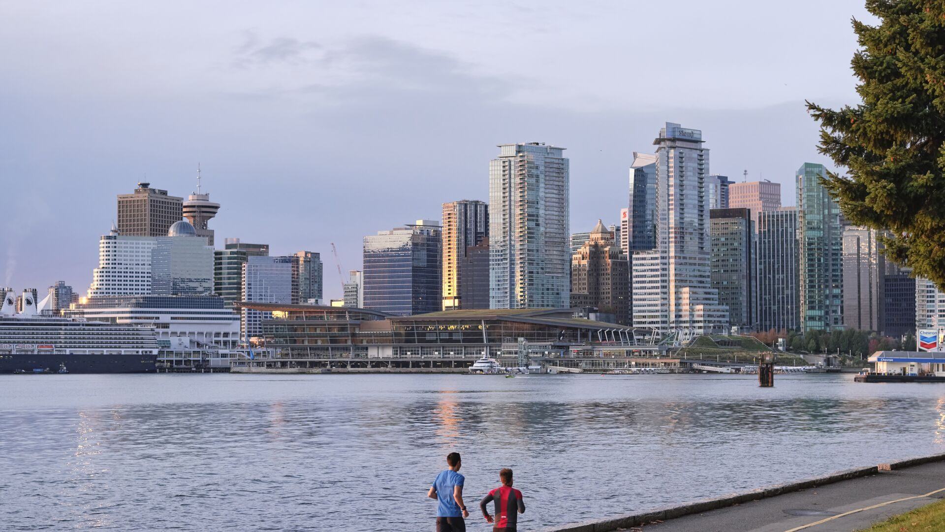 Two people on the Stanley Park seawall facing Vancouver's downtown skyline
