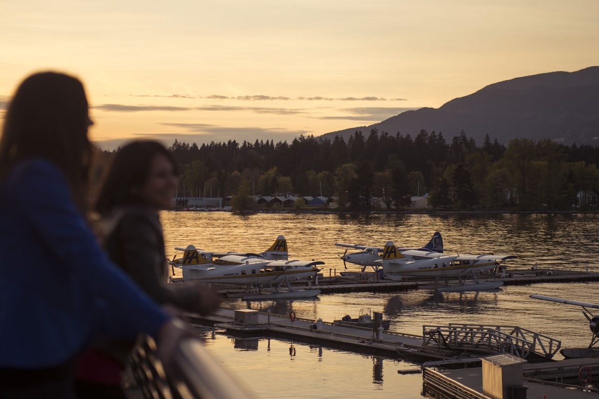 Two people watching seaplanes moored in Vancouver harbour at sunset