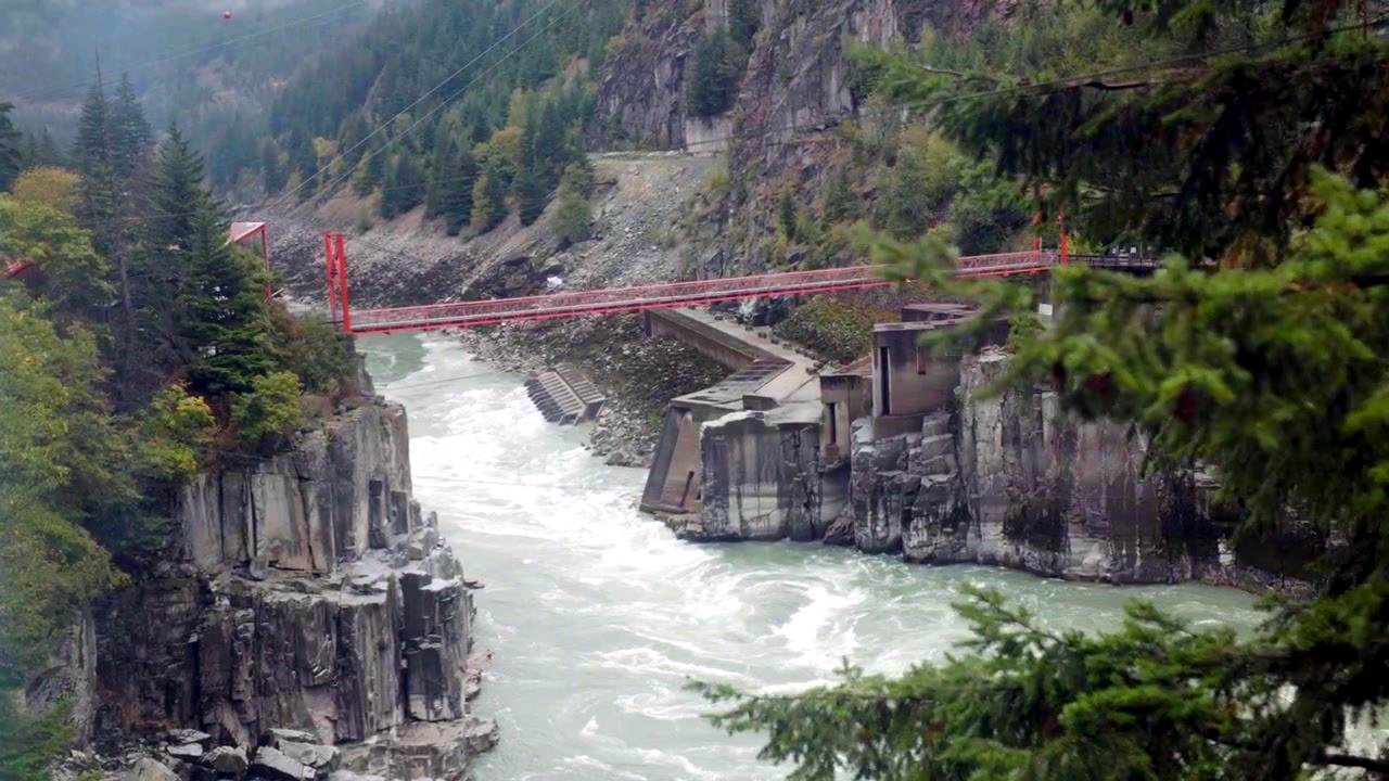 A rushing river between rock walls beneath a red bridge in the canyon