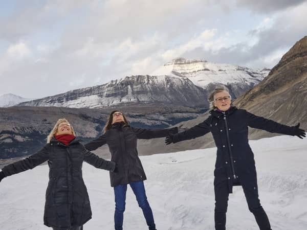 Visitors standing with arms outstretched on the snow at the Columbia Icefield