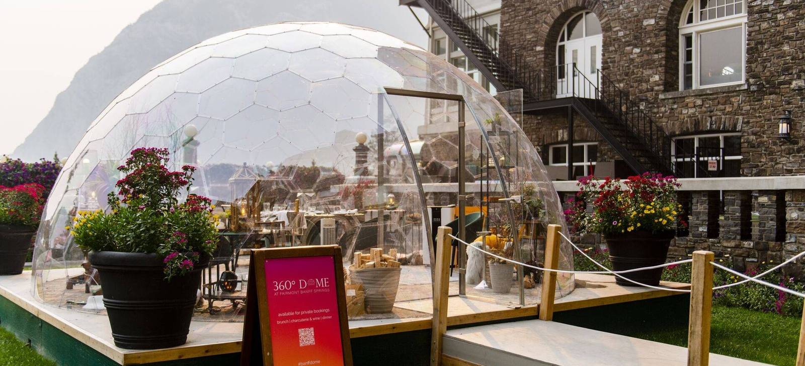 A glass dining dome beside a stone hotel with flower planters