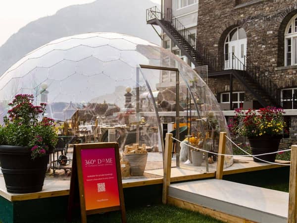 A glass dining dome beside a stone hotel with flower planters