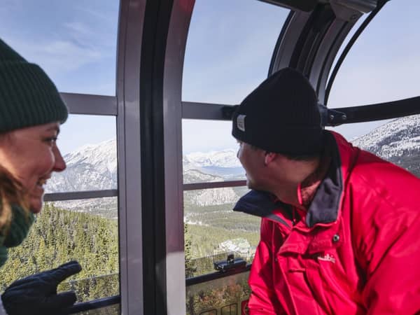 A couple in a gondola cabin looking out at the mountains