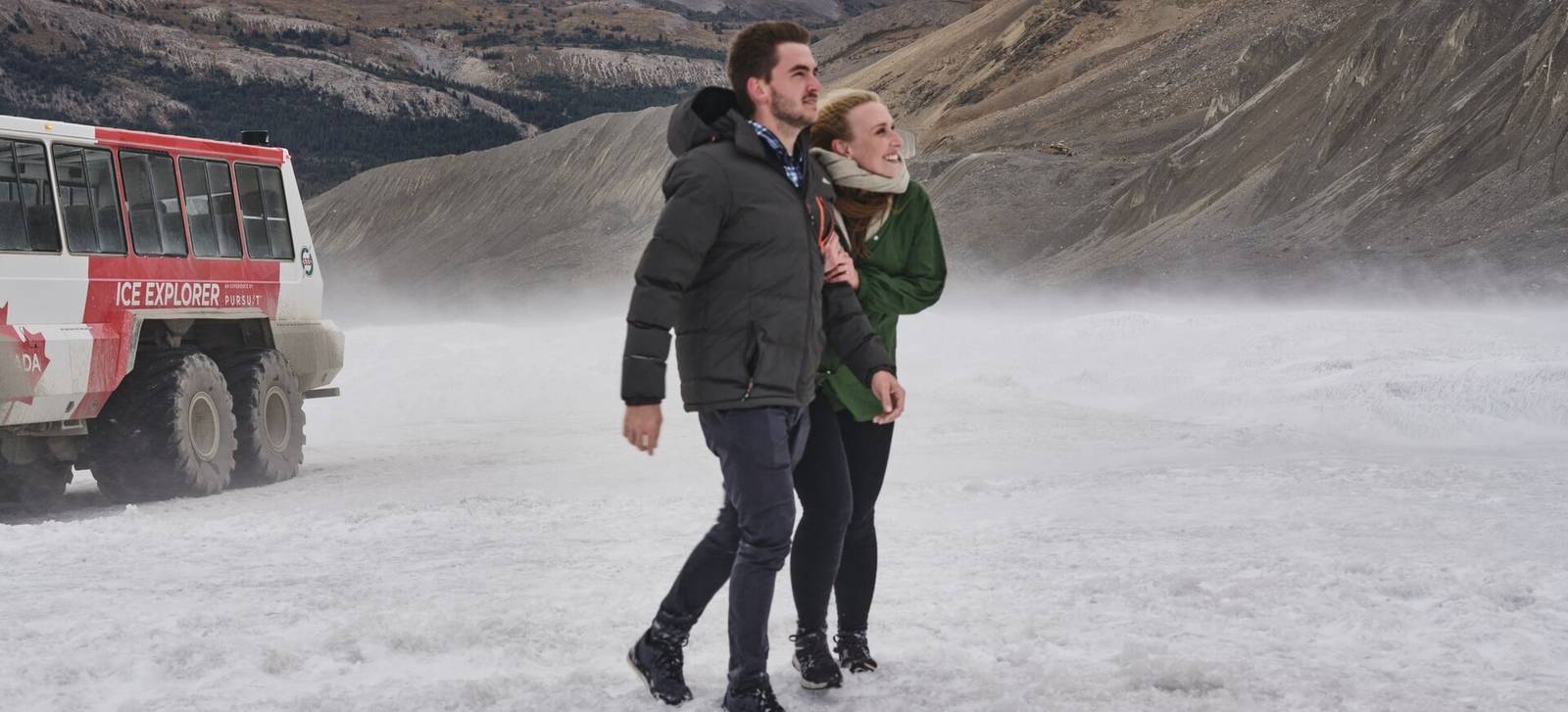 A couple walking on the Columbia Icefield beside an Ice Explorer vehicle