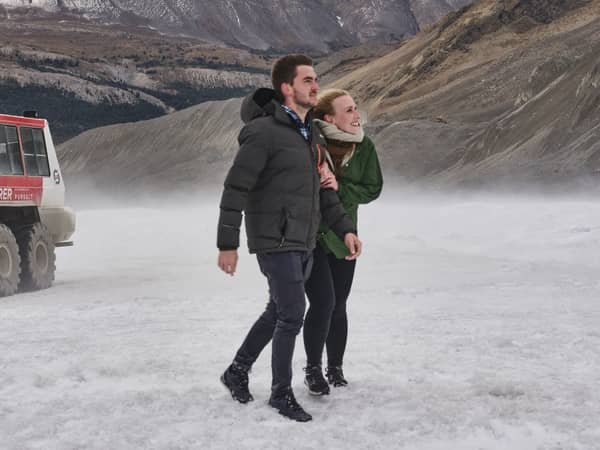 A couple walking on the Columbia Icefield beside an Ice Explorer vehicle