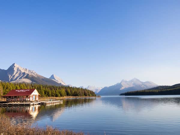 A red boathouse on the shore of Maligne Lake with mountains beyond