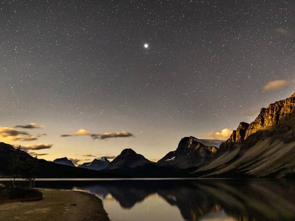 Stars above a mountain ridge and still water at Maligne Lake