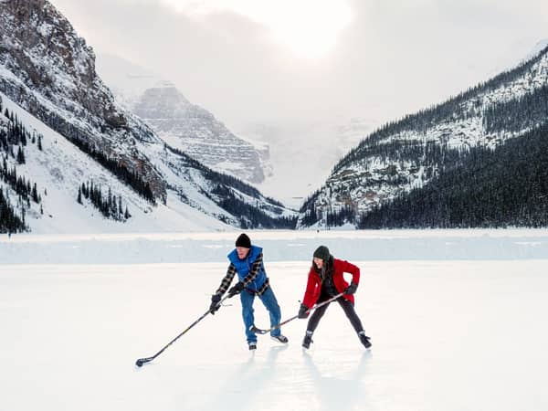 Two skaters on the frozen surface of Lake Louise beneath snowy peaks