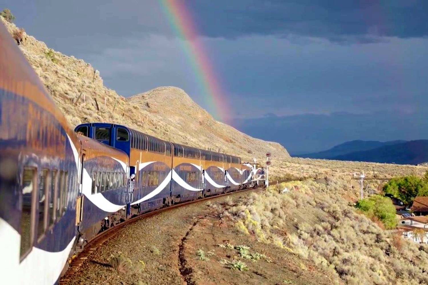The Rocky Mountaineer winding along a sunlit hillside beneath a rainbow