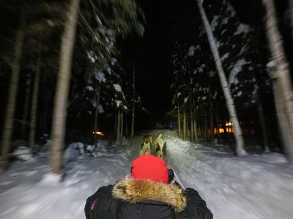A guest in a fur-trimmed red parka riding through a snowy forest at night