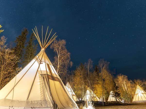 A row of lit tipis under a deep blue night sky