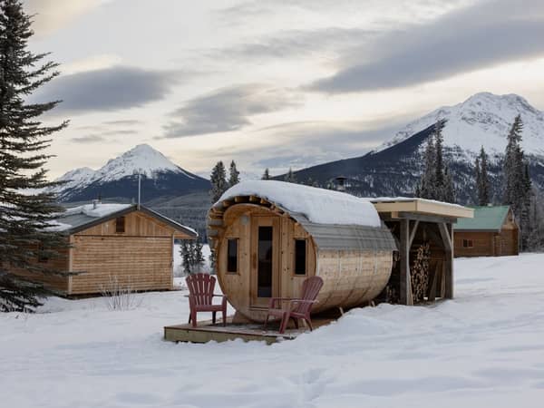 A barrel sauna and cabin in deep snow with mountains beyond