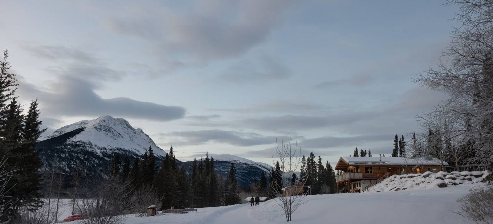 A snowy Yukon lakeshore with cabins and a mountain peak behind